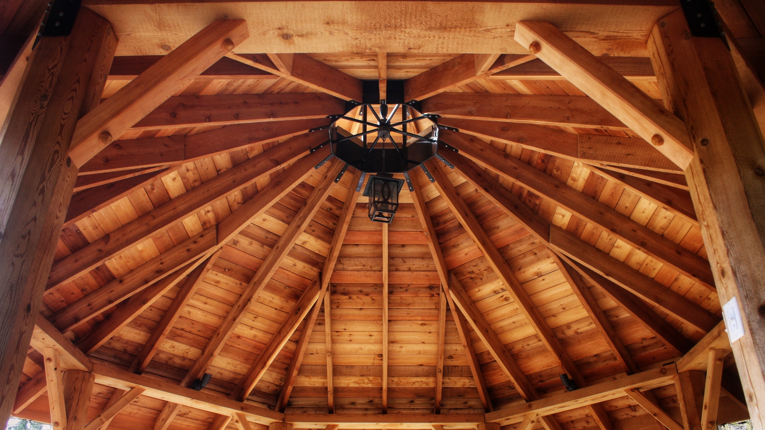 Cedar gazebo roof from below, rafters and posts meeting a steel compression ring